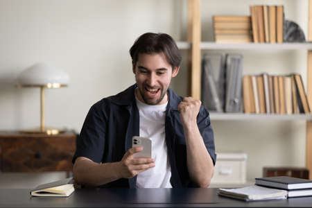 Cheerful excited smartphone user celebrating win, success, achieve, enjoying luck, getting message with good news on smartphone, reading text on screen, making winner yes gesture, laughing, shoutingの写真素材