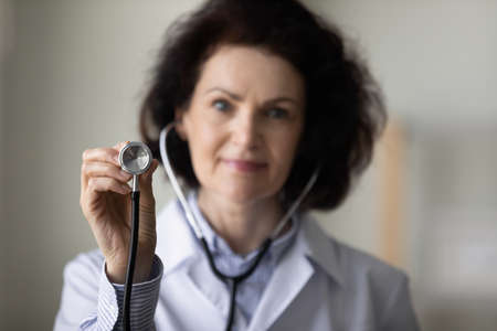 Mature female GP doctor hand holding stethoscope close up object, Practitioner advertising medical examination, routine checkup. Medic care, healthcare conceptの写真素材