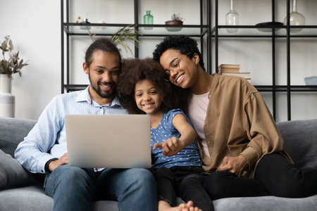 Happy bonding two generations African American family looking at computer screen, watching funny comedian movie or video in social network, choosing goods in internet store, tech addiction concept.の写真素材