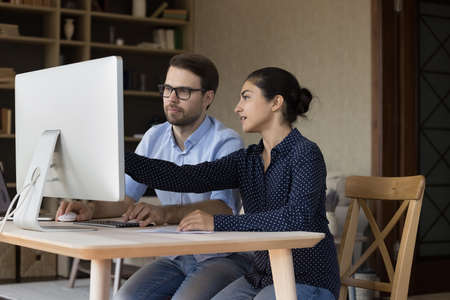 Two focused multiethnic coworkers working on project together, presentation on desktop monitor,...