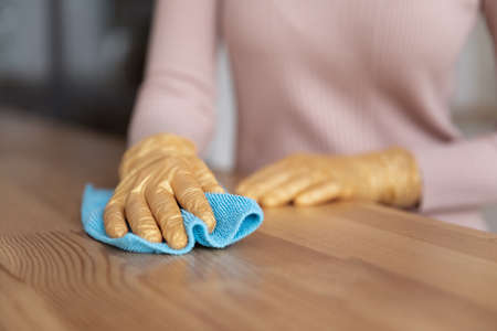 Close up cropped of woman in gloves cleaning wooden table surface, housekeeping service worker, young female housewife doing chores daily routine at home, removing dirt, wiping dust with napkinの写真素材