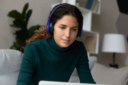 Young Hispanic woman in wireless earphones work online on computer at home. Pensive millennial...