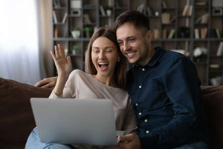 Happy young family couple waving hands, starting video call meeting with friends or family, using computer software application. cheerful millennial bloggers streaming stories for social networks.の写真素材