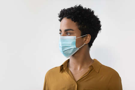 Head shot millennial African American woman wearing disposable medical protective facemask, looking in distance, thinking of coronavirus epidemic end, isolated on white studio background, copy space.の写真素材