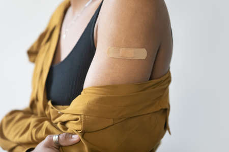 Close up focus on glued patch on arm of young African American woman, isolated on white studio wall background, coronavirus or grippe injection vaccination advertisement, public awareness concept.の写真素材