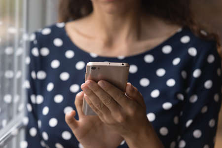 Close up young woman holding cellphone in hands, involved in using mobile software applications, playing internet games, communicating in social networks, buying goods or service shopping online.の写真素材