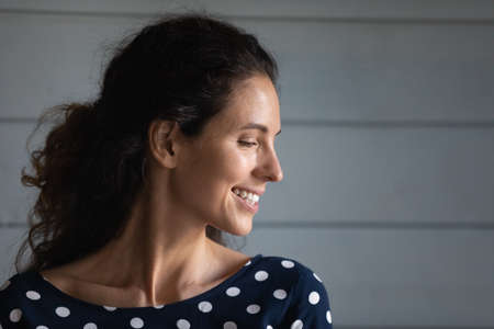 Head shot profile view sincere attractive smiling young latin ethnic woman posing on grey wall...