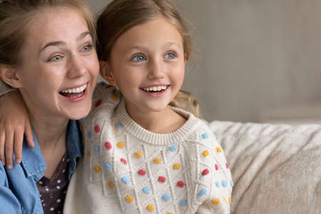 Head shot inspired happy affectionate young mum and small adorable kid daughter looking in distance, enjoying peaceful loving tender carefree moment together at home, copy space for advertising text.の写真素材