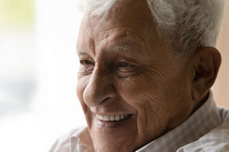 Close up head shot happy old senior retired man showing perfect white teeth looking in distance, dreaming of future, recollecting good memories or thinking of positive life moments, ageing concept.の写真素材