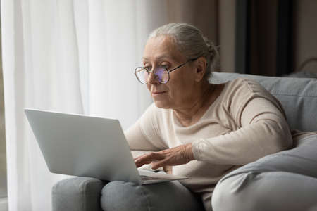 Addicted to modern technology happy middle aged woman in eyeglasses using laptop software applications, enjoying web surfing information, communicating in social network, playing games or shopping.の写真素材