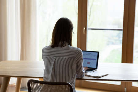 Back of young business woman working at home office workplace table, checking schedule, workday tasks on planner service on laptop screen. Female employee, student girl using online calendar appの写真素材