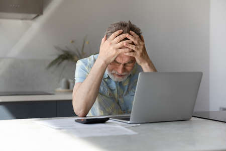 Unhappy frustrated middle aged 60s man holding head in hands, feeling stressed of having financial...