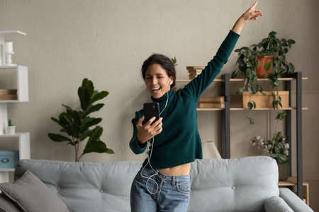 Overjoyed millennial gen beautiful woman dancing, learning moves from educational video on smartphone, recording vlog or having fun choosing audio in modern application, domestic activity concept.の写真素材