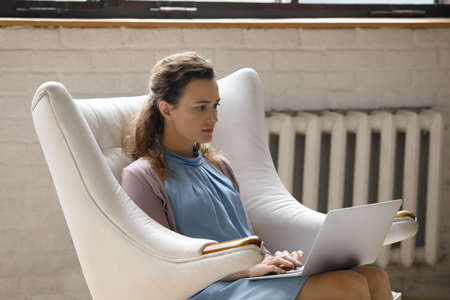 Concentrated young woman working remotely on online project on computer, considering problem...