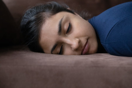 Head shot exhausted young Indian woman sleeping on couch, feeling restless after hard working day, relaxing renewing energy at home, napping daydreaming, watching sweet dreams, fatigue concept.の写真素材