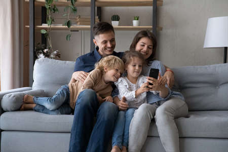 Happy relaxed sincere two generations family looking at cellphone screen, enjoying playing mobile...