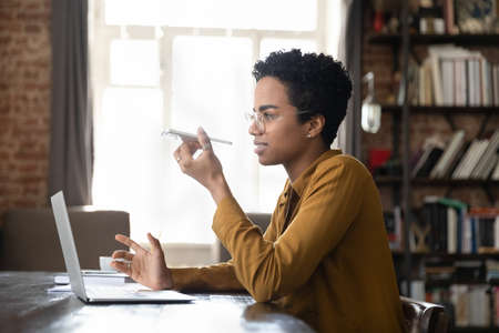 Positive African freelance professional woman having telephone call on speaker, recording audio...