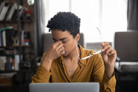 Tired young African freelance employee tired of work at laptop computer in home office, feeling...