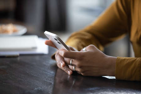 Hands of young dark skinned woman with finger rings using online app on mobile phone, making call,...