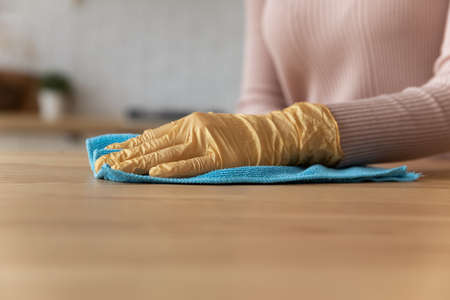 Close up female hand wear rubber latex protective yellow glove cleaning wooden kitchen countertop...