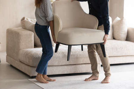 Couple carrying cozy armchair, placing furniture in apartment cropped, barefoot woman and man moving into new home, decorating modern living room together, relocation and interior design conceptの写真素材