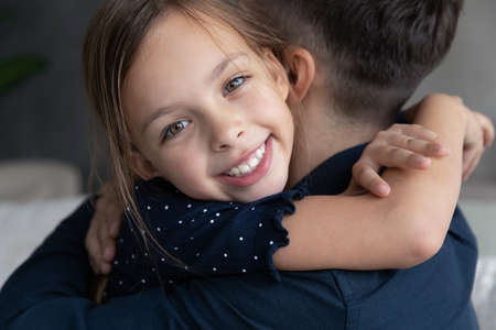 Head shot portrait close up smiling Caucasian 8s girl hugging father, happy adorable daughter child embracing dad, good family relationship, enjoying tender moment together, fatherhood conceptの写真素材