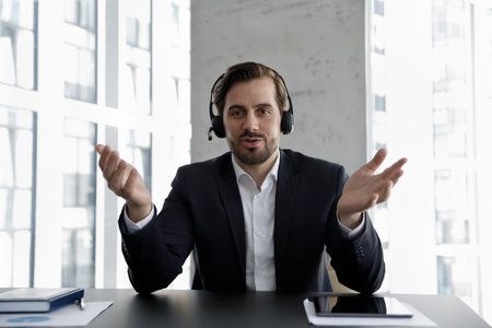 Friendly confident business professional in formalwear, employee, blogger in headphones looking at camera at workplace, speaking on video call, giving consultation. Screen head shot portraitの写真素材