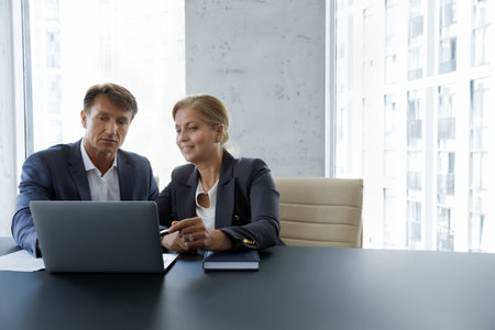 Mature couple of business leaders, top managers, company owners using laptop computer together, discussing work project, monitoring investment stock income, looking at display, talkingの写真素材