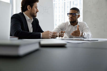 Diverse business partners discussing project at meeting table, sharing ideas. African manager, developer presenting startup to investor. Intern consulting mentor, teacherの写真素材