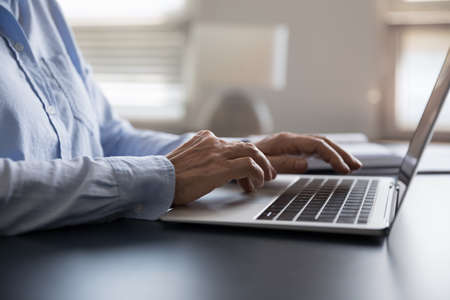 Close up focus on wrinkled hands of elderly businesswoman typing on laptop keyboard, web surfing...