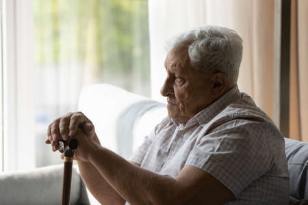 Sad depressed older 80s man holding gimp stick knob, using walking cane, having disability, mobility problems, joints, bones disease. Lonely older patient feeling apathy, loneliness, painの写真素材