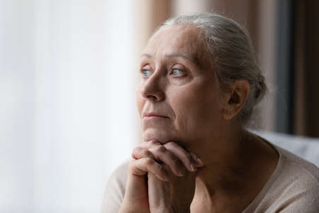 Thoughtful bored older 70s woman looking at window, feeling depressed, frustrated, lonely, suffering form memory loss, dementia, Alzheimer disease, mental disorder. Old age problems conceptの写真素材