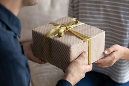 Young man giving gift to beloved woman, girlfriend, wife. Hand of couple holding, taking, receiving...