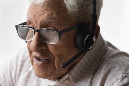 Face of old senior 80s man in glasses, headphones speaking at mic, talking on video call, holding virtual conversation, attending online learning conference, meeting, webinar. Internet communicationの写真素材