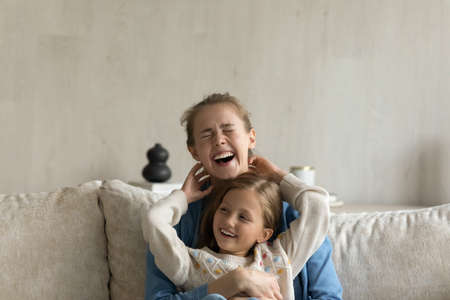 Cheerful giggling kid and young mom hugging, laughing, having fun. Mother holding in arms, cuddling,...