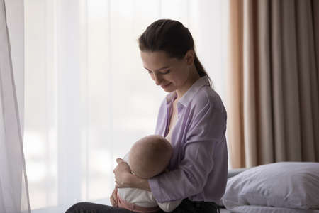 Happy calm young mom enjoying breastfeeding baby, maternity leave, emotional bonding with little...