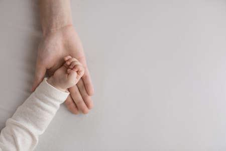 Hand of sweet few month baby resting in mothers palm. Mom holding, touching tiny arm of little sleepy daughter, son. Kid lying on bed with white sheet. Close up, cropped shot. Motherhood conceptの写真素材
