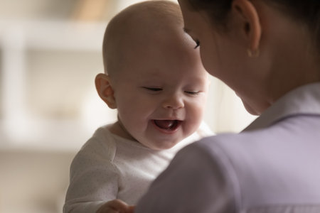 Happy cheerful adorable baby laughing, smiling in young mothers arms. New mom holding little kid, hugging positive child with tenderness, love, care. Close up. Motherhood conceptの写真素材