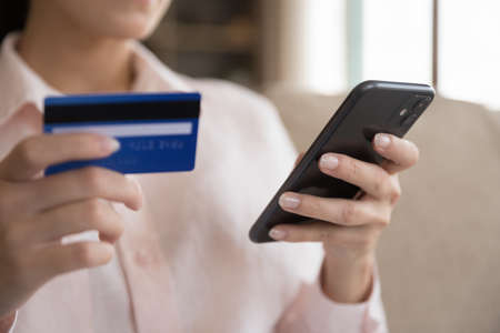 Close up happy young female client holding bank card and smartphone in hands, making payments using mobile e-banking application, shopping online in internet store, purchasing goods or services.の写真素材