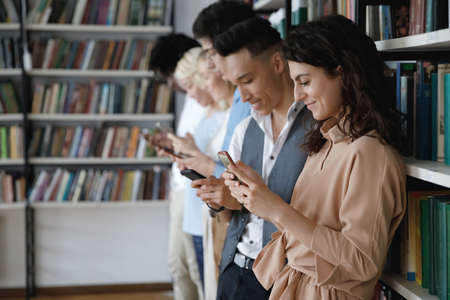 Side view addicted to modern tech happy young diverse students using cellphone apps, enjoying web...