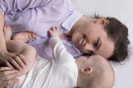 Happy caring devoted new mom enjoying relaxation with infant kid, hugging, cuddling, caressing baby,...