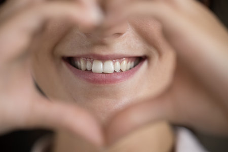 Close up happy young woman making heart sign, showing straight white teeth, feeling with...