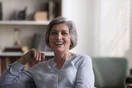 Attractive middle-aged woman relaxing on cozy sofa in living room staring at camera looks peaceful, feels happy, spend leisure alone at home. Homeowner portrait, carefree life on retirement conceptの写真素材