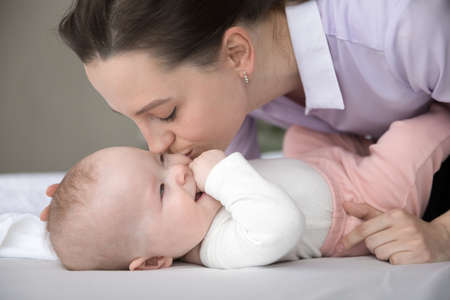 Close up young affectionate loving happy Caucasian mother kissing cheek of adorable laughing sweet...