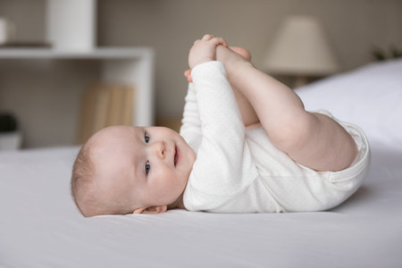 Full length carefree joyful small adorable kid boy girl touching little toes, enjoying playing with...