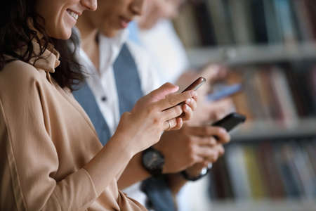 Group of young teen people standing indoor with smartphones in hands, chatting in social media, ignoring live communication prefer virtual, close up view. Gen Z and wireless gadgets overuse, bad habitの写真素材