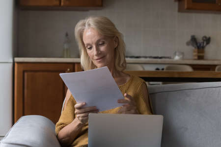 Happy satisfied mature landlady woman reading paper mail letter with good news, reviewing insurance,...
