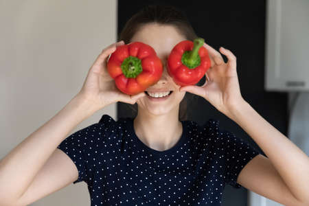 Keep diet, healthy eating, vegetarian lifestyle, eyesight vision check up services concept. Young woman cover her eyes holds two red fresh paprika like eyewear smile pose at camera, head shot portraitの写真素材