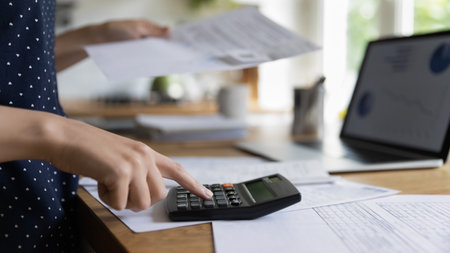 Close up cropped view, table with heap of bills, laptop and unknown female hand using calculator makes calculations, lead personal or company finances, working at home. Savings, accounting conceptの写真素材