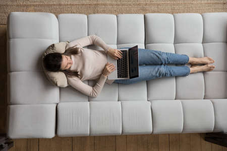 Focused student girl using laptop at home, resting on couch. Distant freelance worker, professional woman working at computer from home, typing, watching movie. Communication concept. Top viewの写真素材